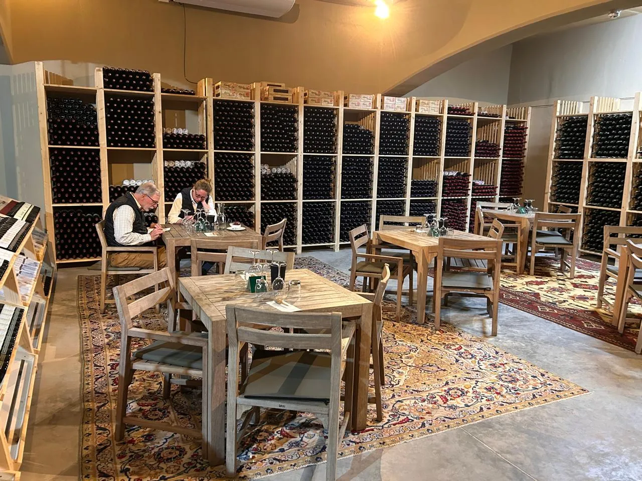 Guests tasting at wooden tables surrounded by floor-to-ceiling walls of bottles in a Robertson estate cellar